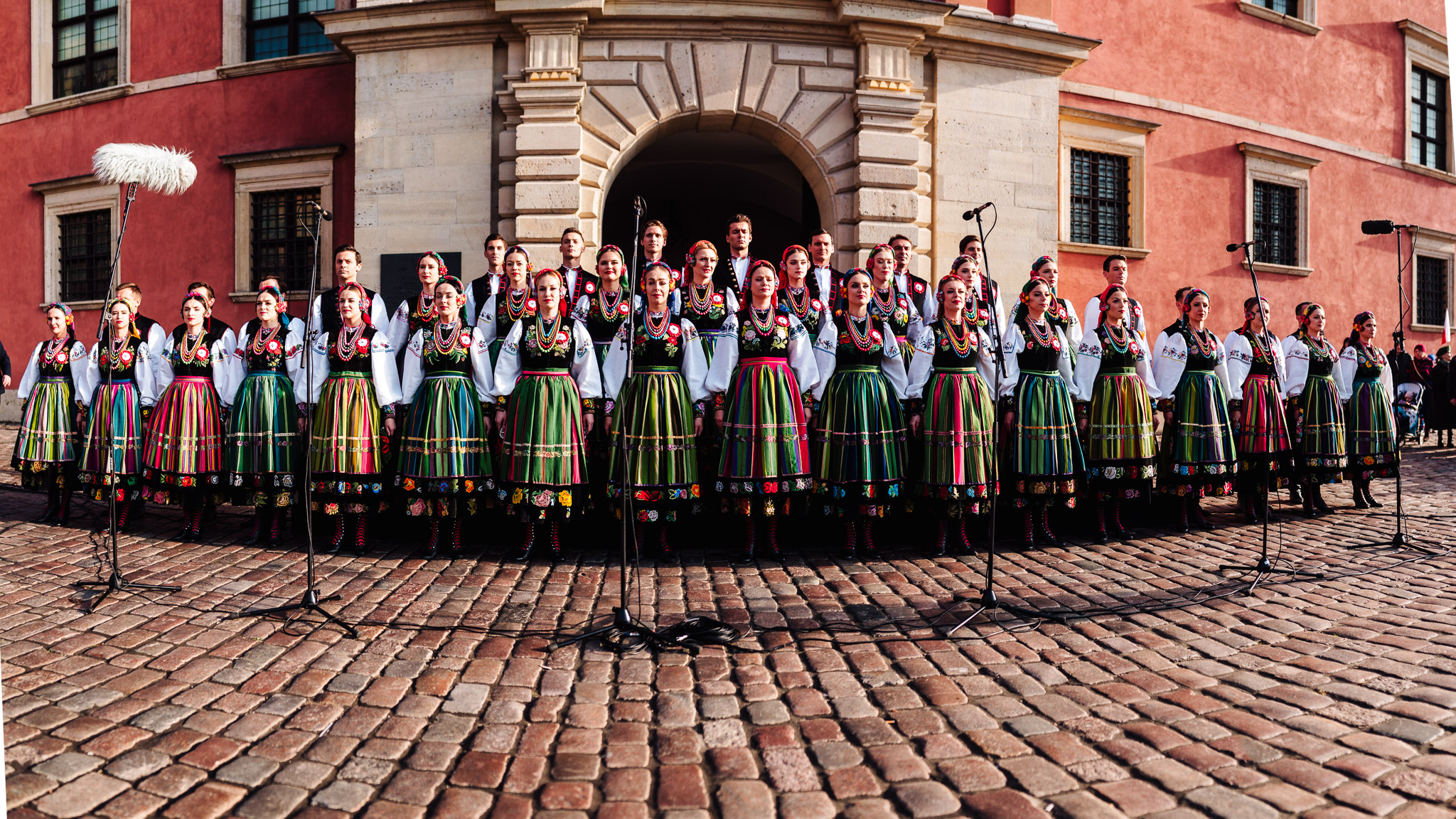 Women in folk costumes lined up in front of the Royal Castle in Warsaw, ready to sing the national anthem