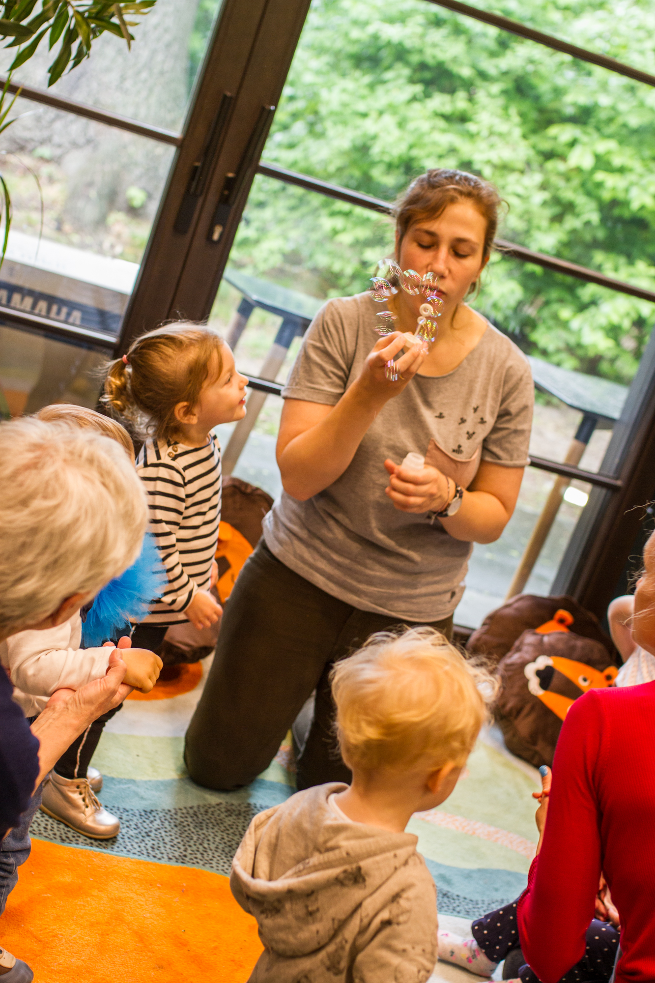 A bubble entertainer playing with young children on the mat around her. 