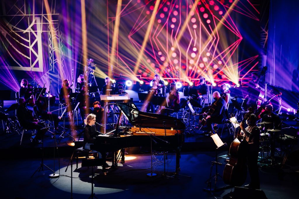 An illuminated stage with musicians, with a grand piano in the foreground