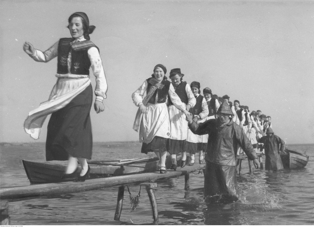 A black and white archival photograph showing women in folk costumes stepping off a boat.