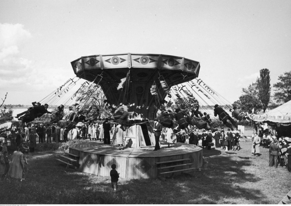 karuzela w ruchu, na niej bawiący się ludzie, dookoła obserwatorzy