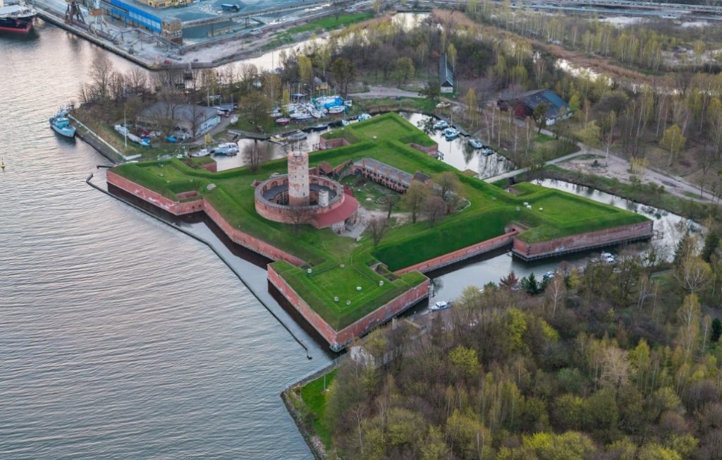 twierdza w formie czteroramiennej gwiazdki obok rzeki, otoczona fosą, w jej środku ceglane zabudowania