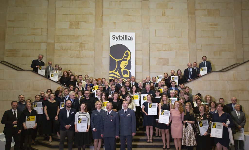 na schodach stoi grupa laureatów trzymając w rękach dyplomy i wyróżnienia