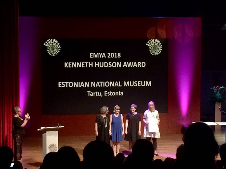 czworo ludzi na podium, prezentują odbieraną nagrodę, w tle napis opisujący muzeum