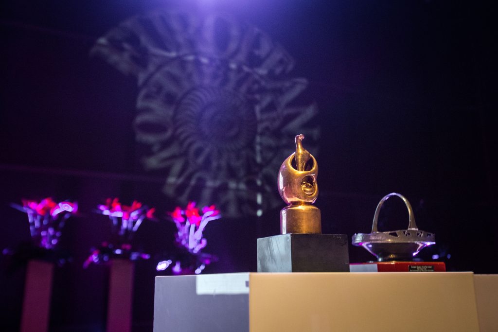 złota statuetka, fioletowe tło ze znakiem emya