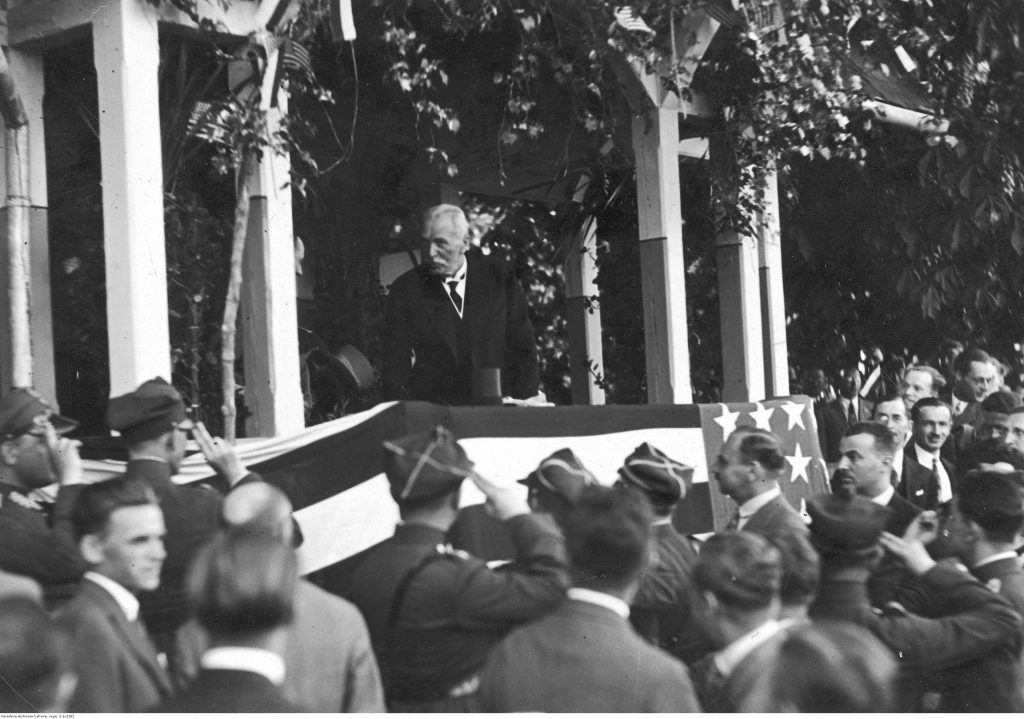 prezydent stoi na trybunie ozdobionej flagą amerykańską 