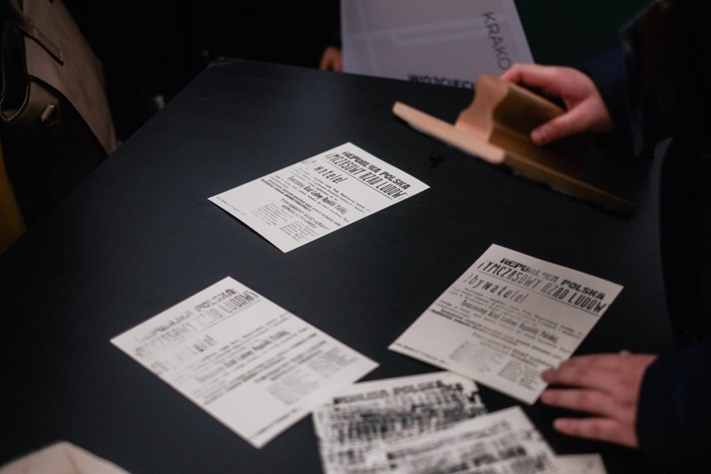 ludzie wokół stołu odbijają pieczątkami odbitki odezwy tymczasowego rządu ludowego