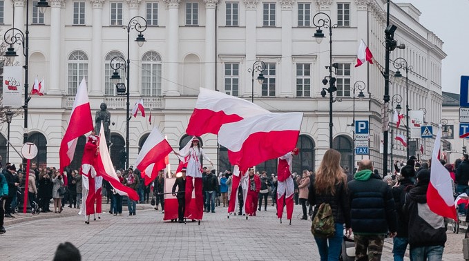 grupa szczudlarzy w biało-czerwonych strojach paraduje po ulicy