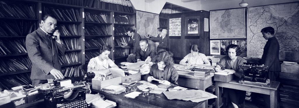 grupa ludzi w pracowni pochylonych nad materiałami archiwalnymi 