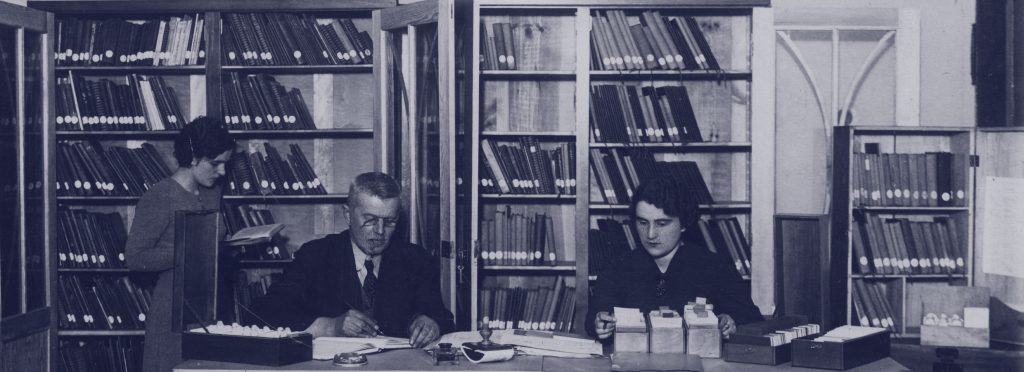 pracownicy przy biurku z rozłożonymi archiwaliami