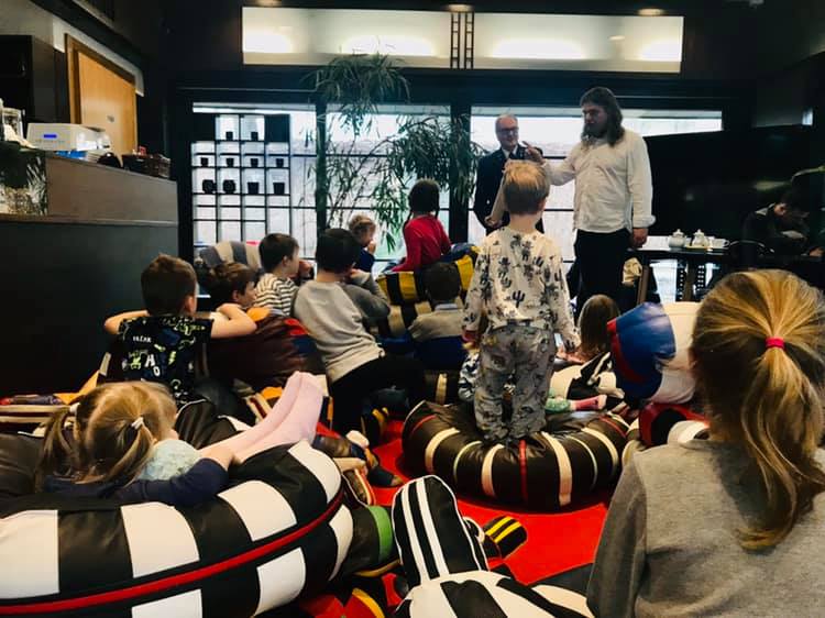 grupa dzieci sziedzi na poduchach i słucha prowadzącego