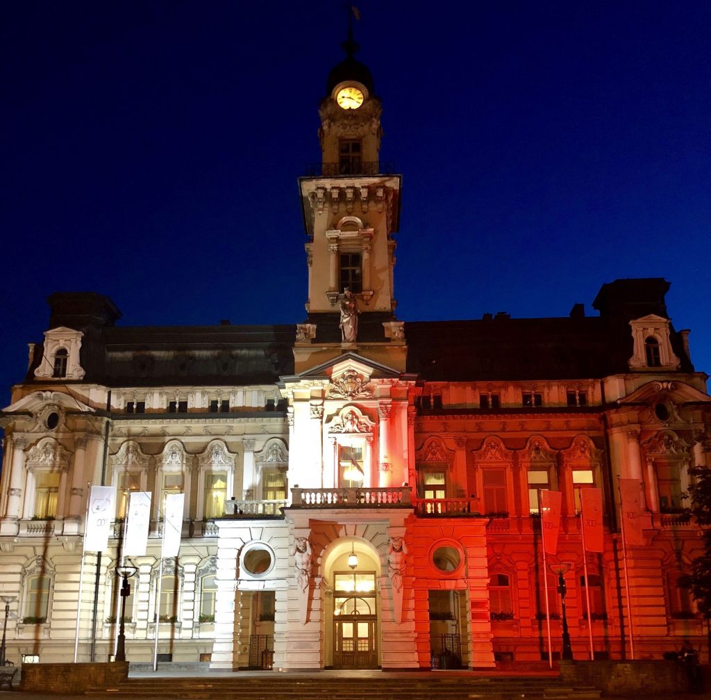 eklektyczny ratusz z wieżą po środku, strona lewa podświetlona jest na biało, prawa na czerwono - w kolorach polskiej flagi