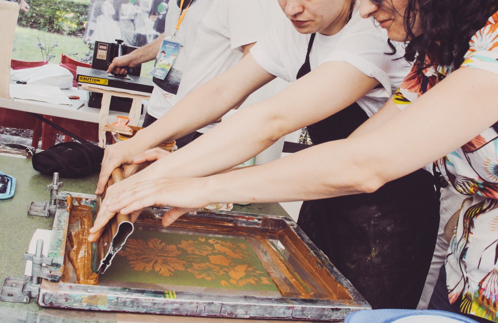 ręce dwóch osób i maszyna do sitodruku w trakcie przenoszenia wzoru