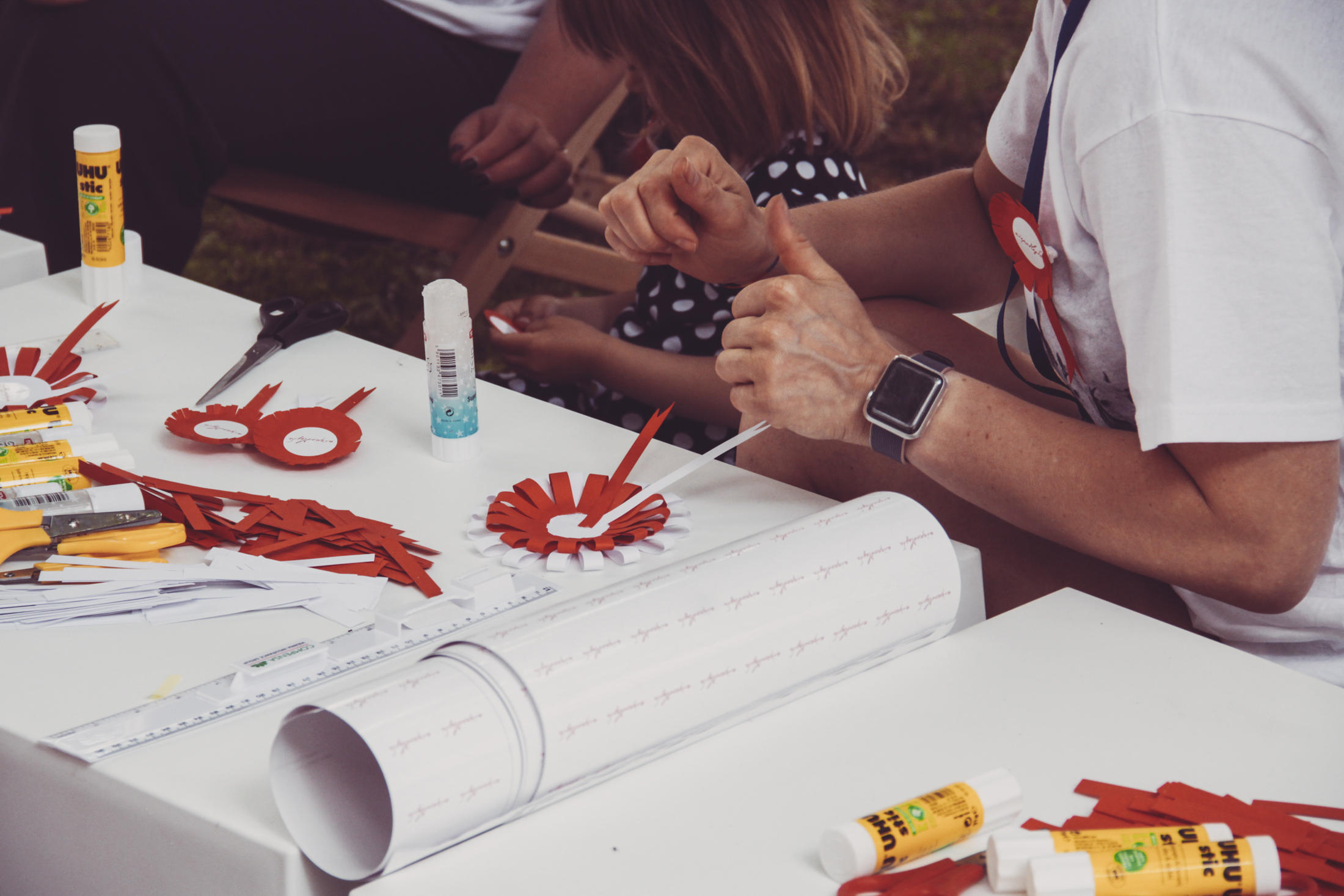 przy stole osoby lepiące kotyliony z przygotowanych elementów