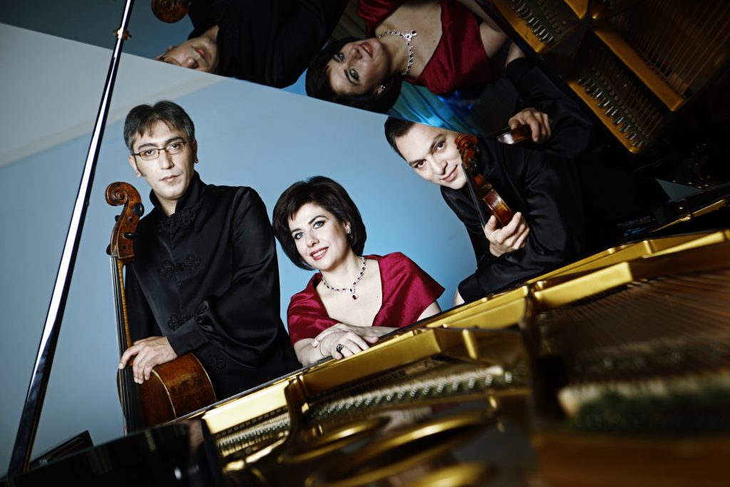 trójka wykonawców przy fortepianie, odbijają się w wypolerowanej pokrywie instrumentu