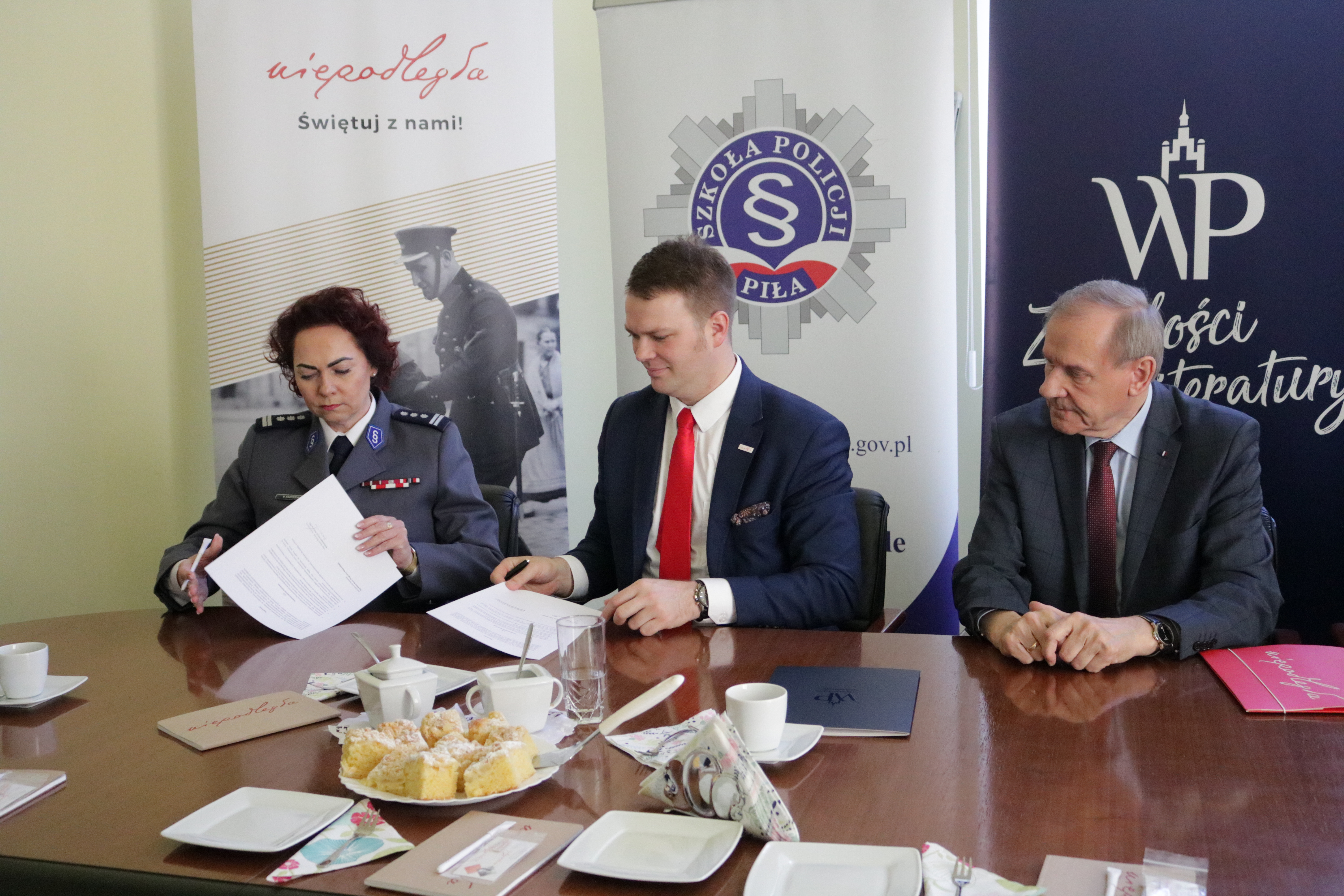 zdjęcie trzech siedzących osób, podpisujących dokumenty