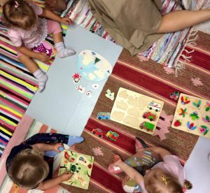 małe dzieci siedzące na dywanikach z rozłożonymi zabawkami edukacyjnymi