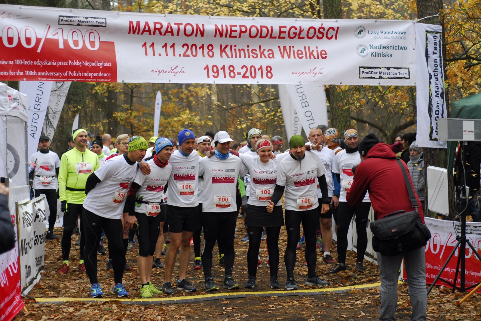 6 sportowców w koszulkach z logo projektu pozuje do zdjecia pod bramą startową maratonu