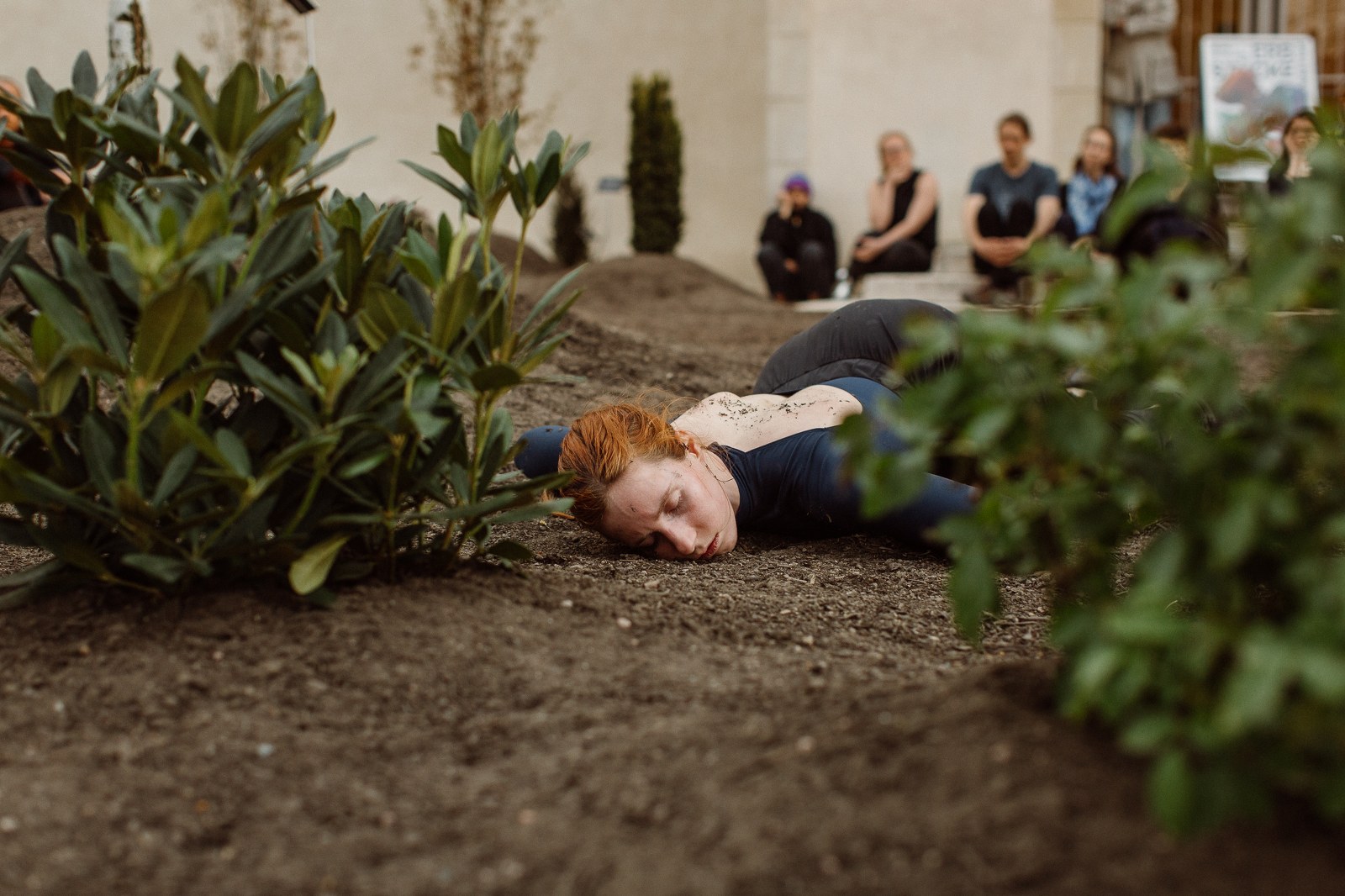 fotografia ze spektaklu tanecznego, rudowłosa tancerka leży na ziemi w otoczeniu roślin