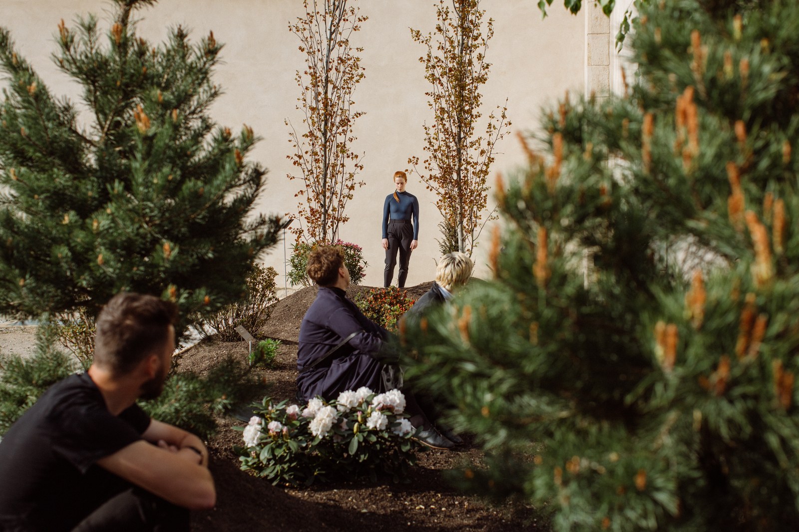 fotografia ze spektaklu tanecznego, scenografią jest ogród, mężczyzna siedzi i spogląda na widoczną w oddali sylwetkę tancerki