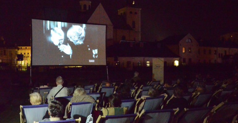 fotografia przedstawiająca widzów na leżakach oglądających projekcję filmu w kinie plenerowym
