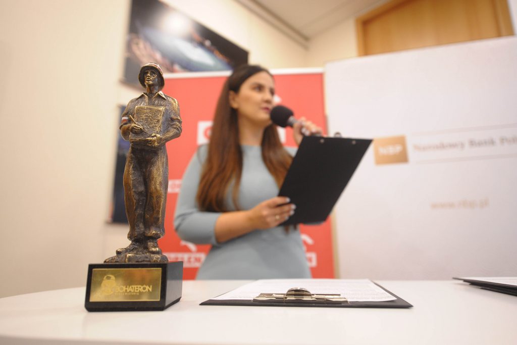 fotografia przedstawiająca statuetkę nagrody BohaterON, w tle sylwetka prowadzącej konferencję prasową