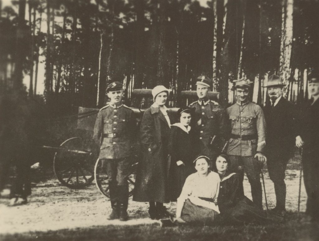 grupa kobiet i mężczyzn pozujących do fotografii w lesie, za nimi samochód