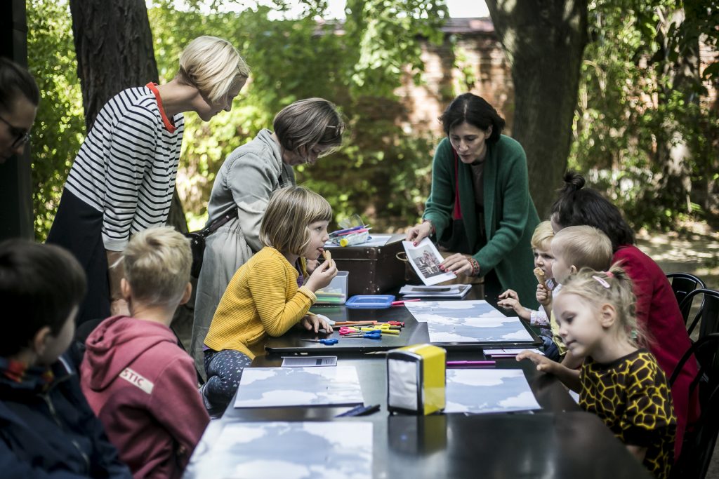 dzieci siedzące wokół stołu, wokół dorosłe kobiety prowadzące warsztaty 