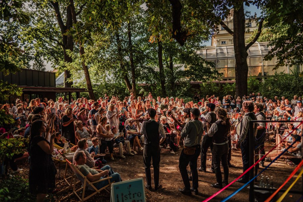 grupa ludzi zgromadzona w parku, obserwująca i śpiewająca wraz z zespołem muzyków