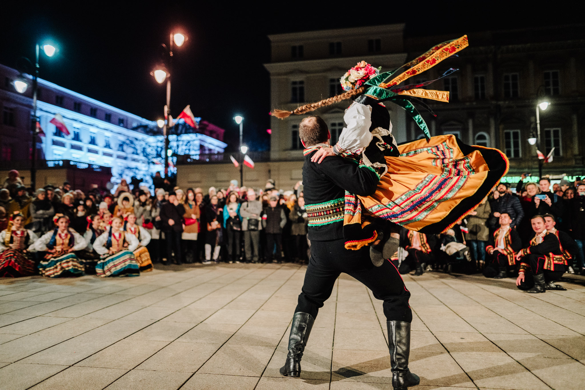 Na pierwszym planie. tańcząca para w strojach ludowych, w tle widzowie