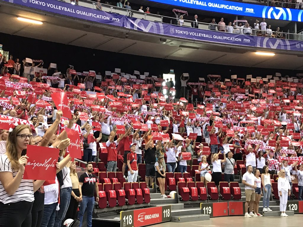 Kibice na trybunach podczas śwpiewania hymnu z uniesionymi kartkami kartoniady