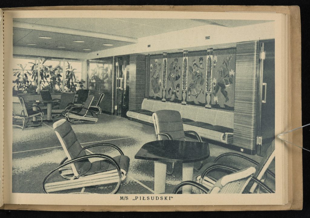 na pierwszym planie stolik z krzesłami, na ścianach werandy obrazy, w tle rośliny doniczkowe