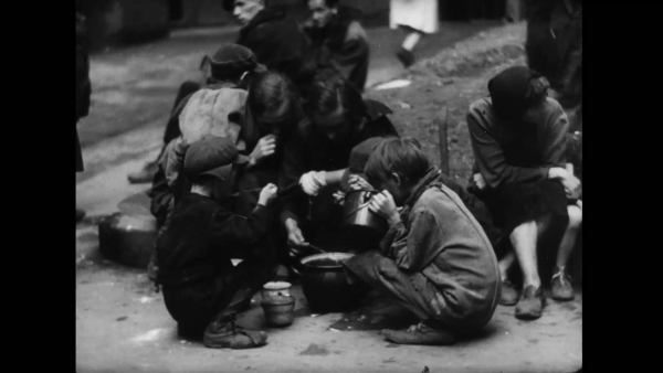 dzieci siedzą na ziemi i jedzą ze wspólnych naczyń