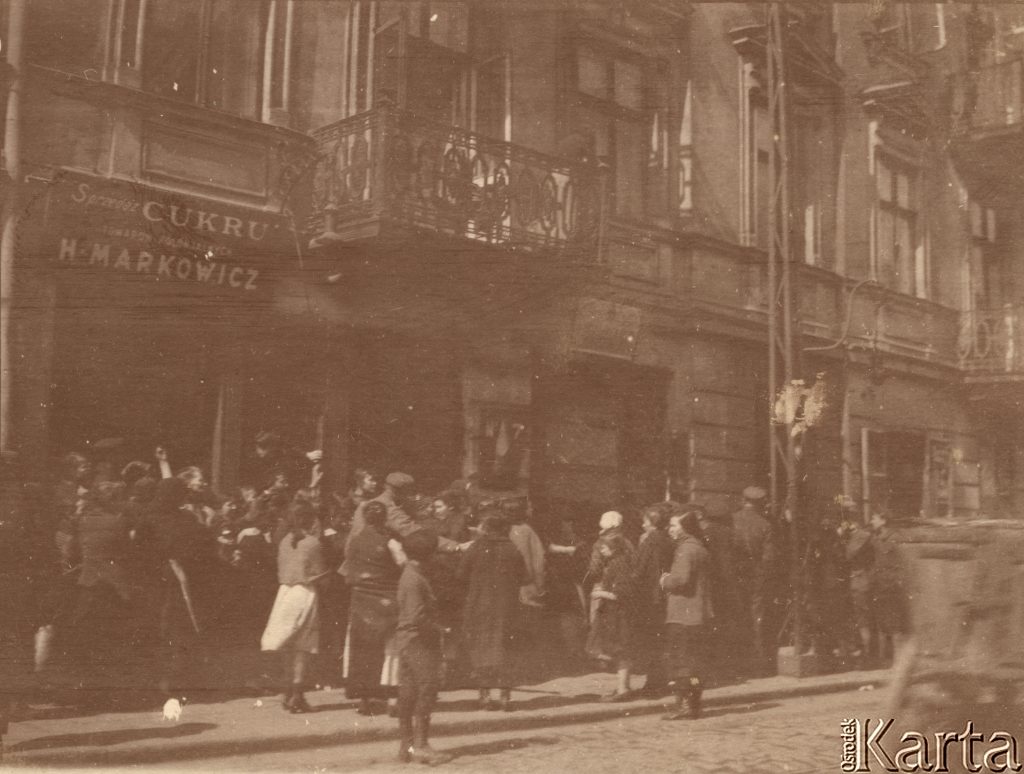 tłum ludzi czekających na ulicy na wejście do piekarni w przyziemiu kamienicy