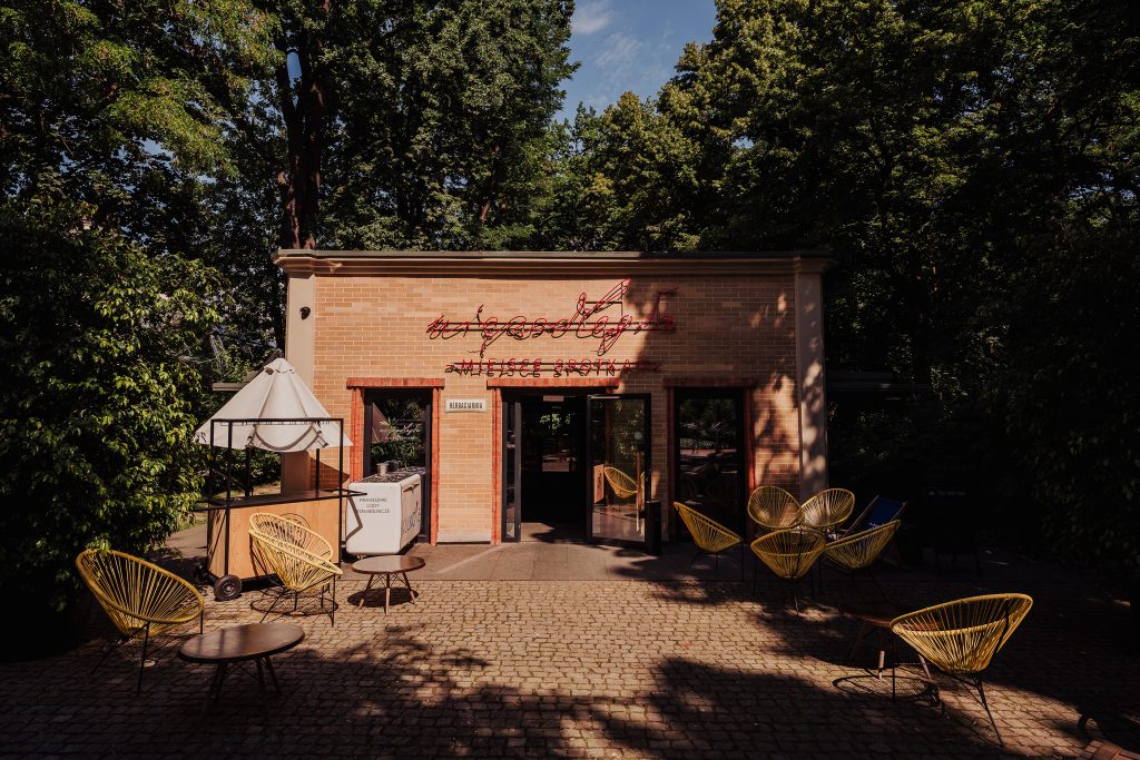 Pawilon kulturalny "Niepodległa. Miejsce Spotkań" od frontu z neonem, w tle drzewa