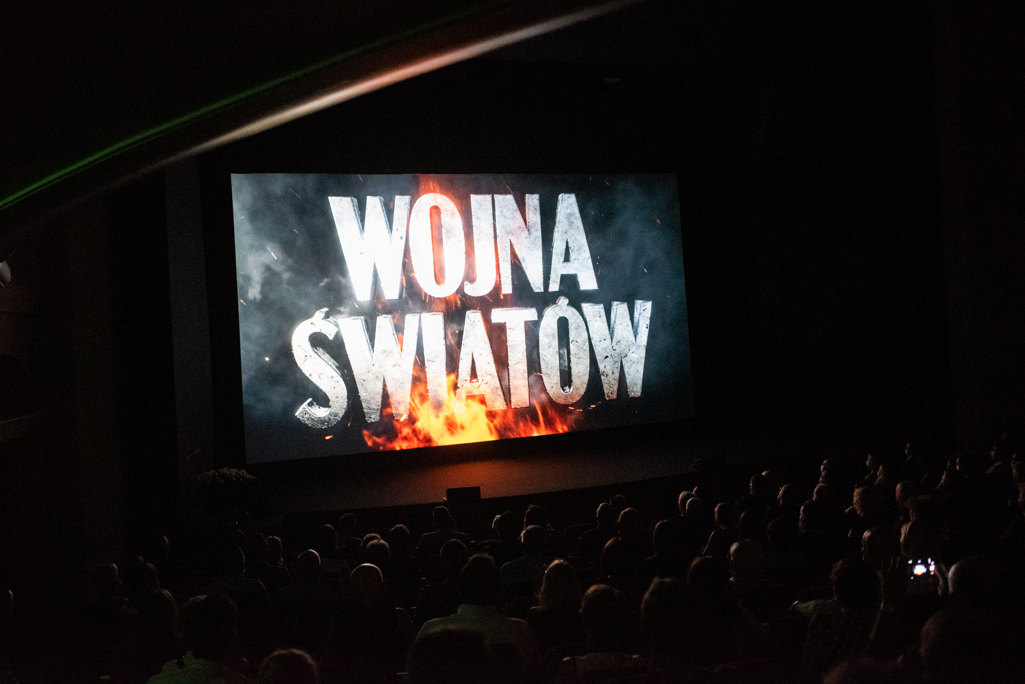 na scenie wyświetlany film z planszą tutułową, rozbłyski na konturacj sylwetek na widowni