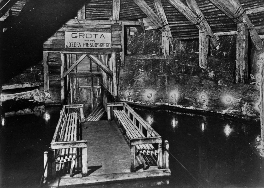 podziemna grota zalana zodą, na wodzie prom z ławeczkami, nad wejściem do groty napis Grota im. Józefa Piłsudskiego