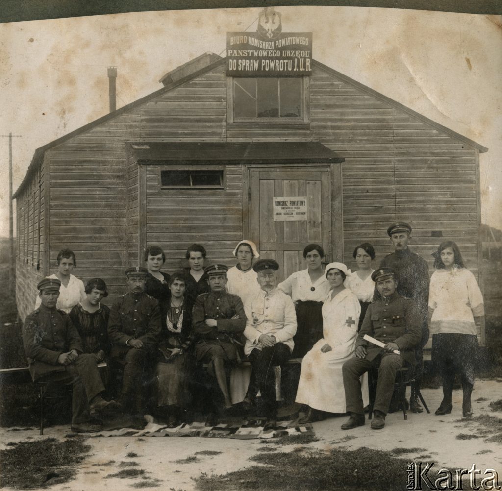 grupa ludzi pozująca do zdjęcia przed drewnianym dużym budynkiem