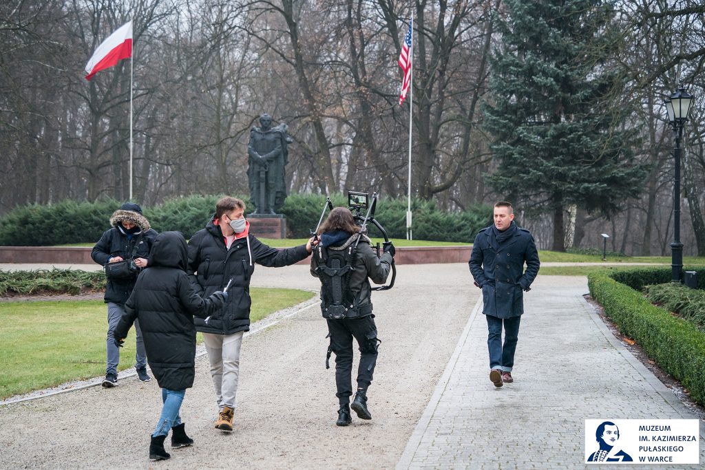 nagruwanie filmu, ekipa idzie tyłem filmując spacerującego aktora w płaszczu