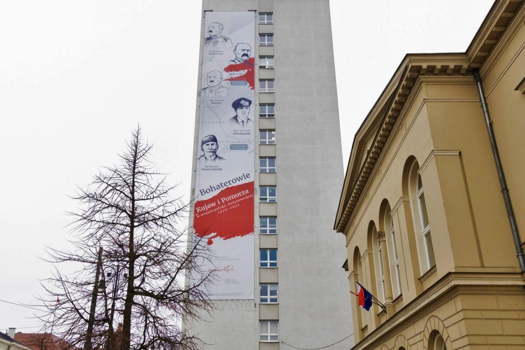 pionowy baner na wysokość kilku pięter, na nim braficznie 5 twarzy bohaterów. Na dole loga.