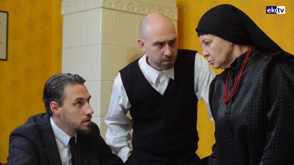 trzech aktorów, dwóch mężczyzn i kobieta podczas rozmowy, ubrani w międzywojenne stroje