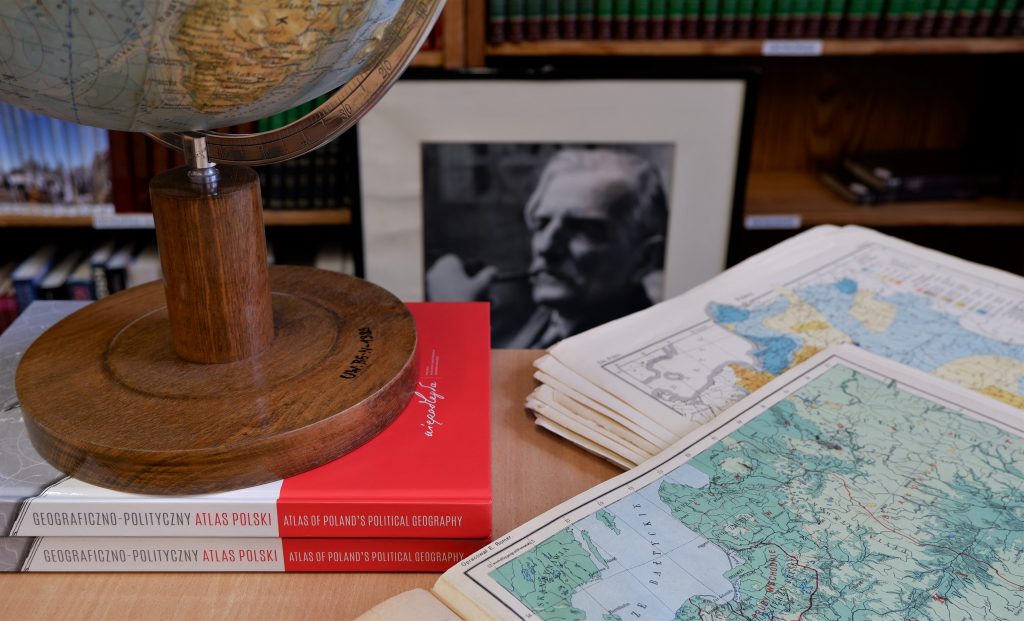 globus i rozłożone mapy, w tle czarno-biały portret Romera