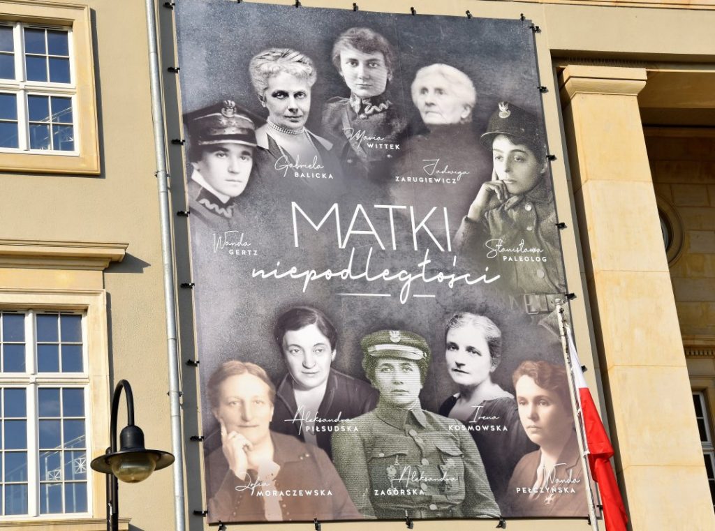 baner z 10 podpisanymi postaciami kobiecymi zawieszony na budynku