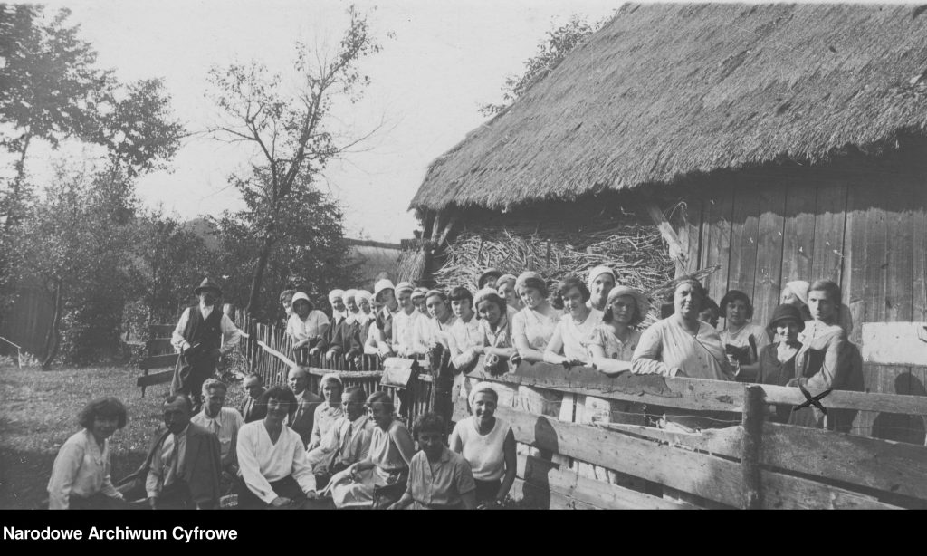 duża grupa ludzi pozująca przy ludowej chałupie