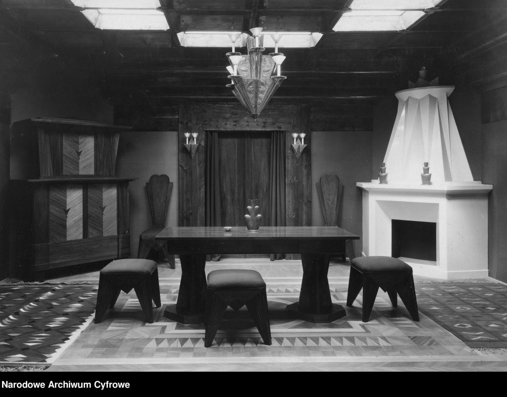 wystój wnętrza - komoda, stół z krzesłami, kominkiem, dywanem i ozdobnym żyrandolem