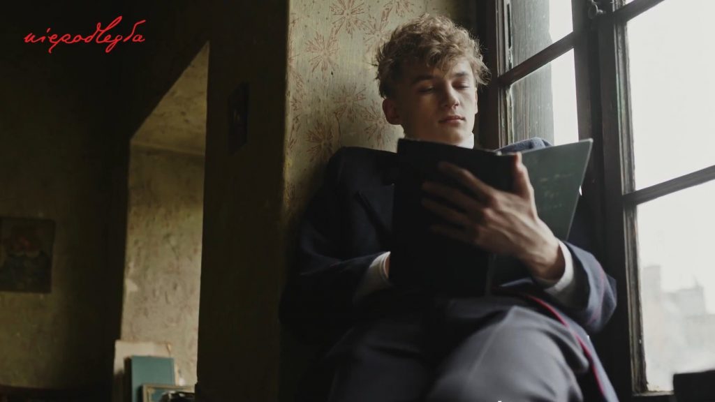 chłopak na parapecie okna czyta Pana Tadeusza trzymanego w rękach