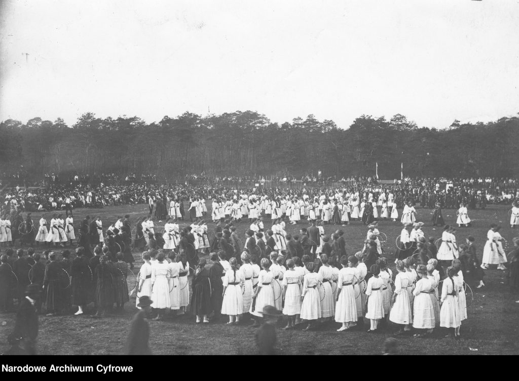 grupy ludzi w odświętnych strojach prezentują się na arenie uroczystości