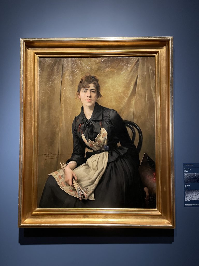 obraz kobiety pozującej w sukni z fartuchem i pędzlami w złotej ramie