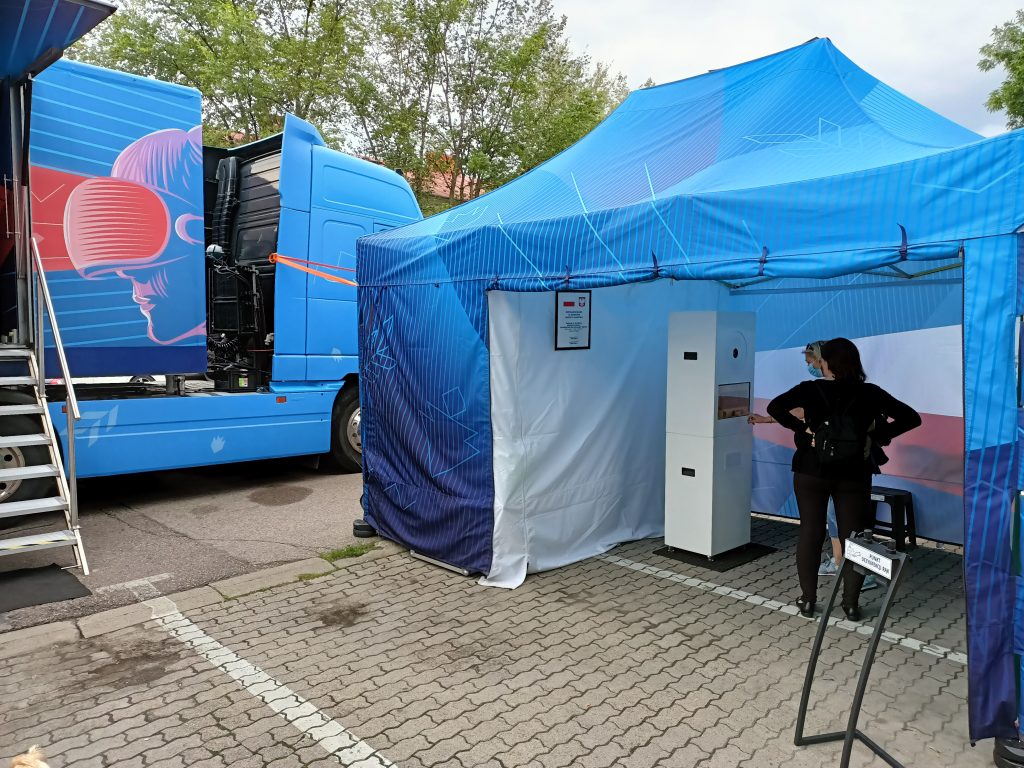 rozstawiony bus i namiot z fotobudką na parkingu, w tle drzewa