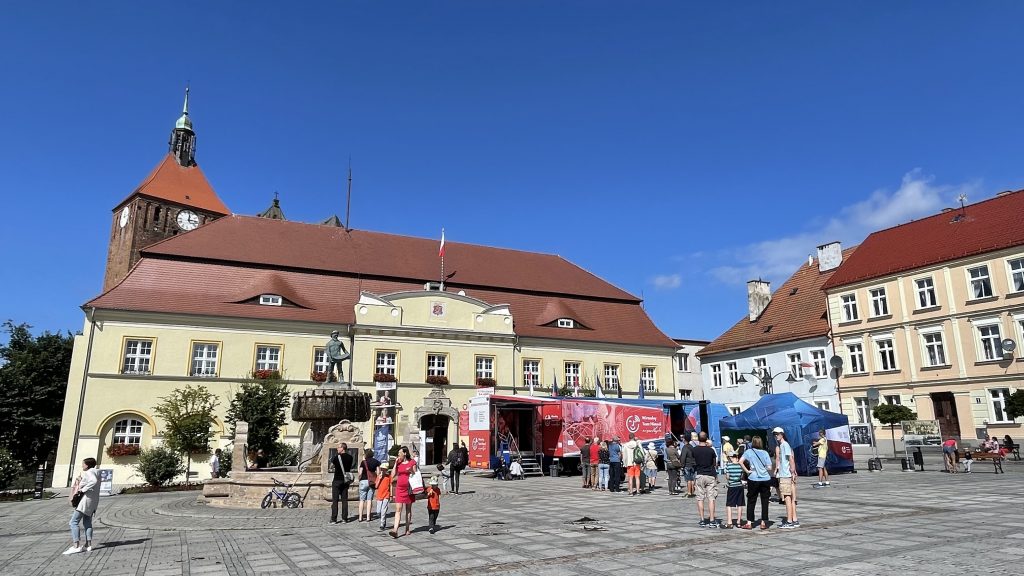 autobus na tle komieniczek rynku w darłowie, w tle wieża kościoła